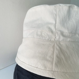 Detail of cream bucket hat featuring textured twill fabric and premium embroidered TK logo