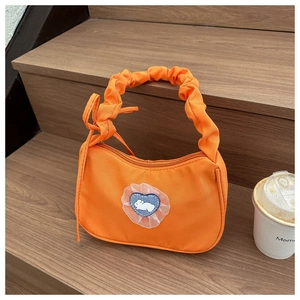 Detail of orange nylon shoulder bag featuring a cute rabbit patch and pleated strap