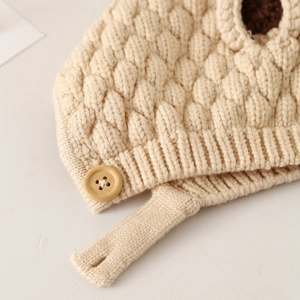 Detailed macro view of beige knit baby hat featuring honeycomb texture and wooden button