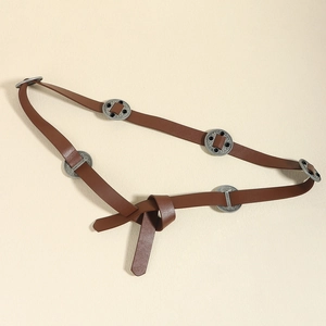 Detail of brown leather belt with ornate metal discs and black gemstones on beige surface