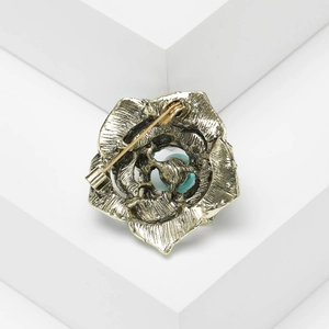 Detail view of vintage bronze flower brooch with turquoise bead and secure back pin