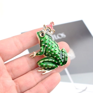 Detailed view of frog brooch with red crown and green enamel finish held in hand