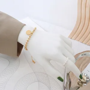 Elegant gold beaded chain bracelet with round tag worn by model in a luxury setting