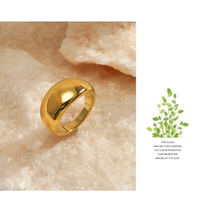 Close-up of a wide polished gold ring placed on a textured beige stone with warm lighting