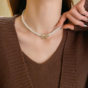 Gros plan d'un collier de perles avec pendentif arc doré porté au cou