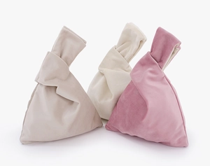 Close-up of three soft velvet knot wrist bags in beige cream and pink colors