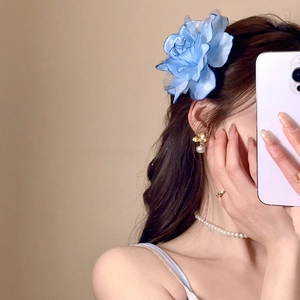 Close-up of blue fabric flower hair clip styled with elegant pearl jewelry and rings