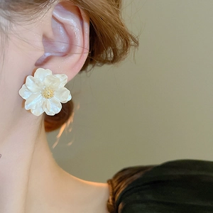 Close-up of white resin camellia stud earring with golden stamen on a model's ear