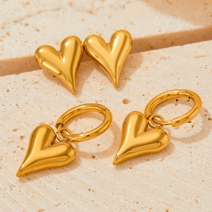 Polished gold heart stud and hoop earrings set on beige travertine stone background