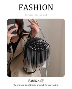 Detail of a black round crossbody bag featuring silver studs and long metal chain tassels