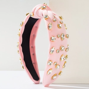 Détail d'un serre-tête en tissu rose noué avec des strass brillants et montures dorées