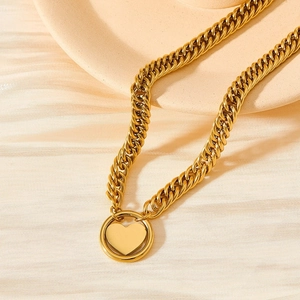 Gold Cuban chain necklace with heart pendant on a minimalist textured background