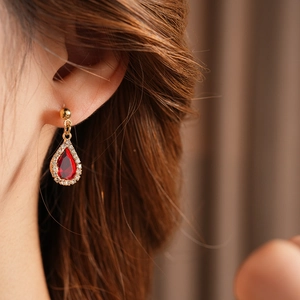 Close-up of gold drop earrings featuring a red gemstone and sparkling diamond halo