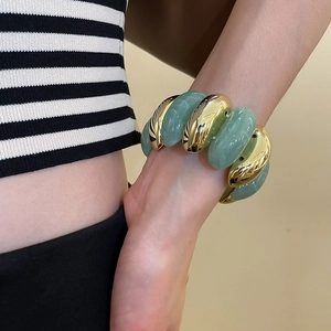 Detail of wide stretch bracelet with chunky gold beads and pale green resin stones