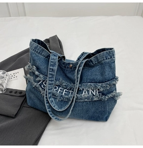 Détail du cabas en jean bleu avec bords effilochés et broderie sur un drap blanc