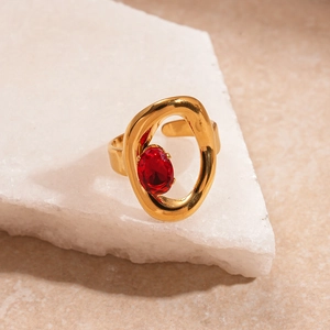 Dettaglio dell'anello dorato irregolare con zircone rosso su sfondo di pietra bianca