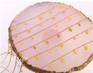 Detail of six gold-plated necklaces with star, heart, and evil eye pendants on pink stone