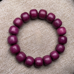 Close-up of violet wooden barrel bead bracelet on a light brown linen background