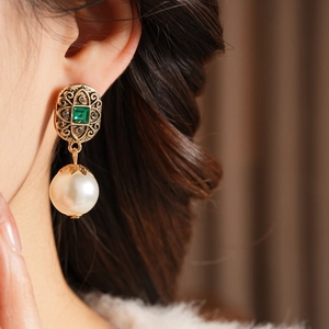 Dettaglio di orecchini vintage in oro con pietre preziose verdi e perle bianche su modella