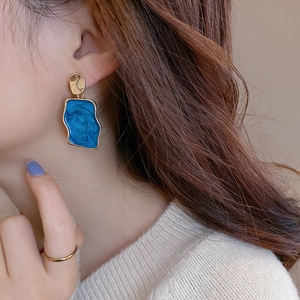 Dettaglio di orecchini geometrici blu con eleganti perni dorati e trama marmorizzata