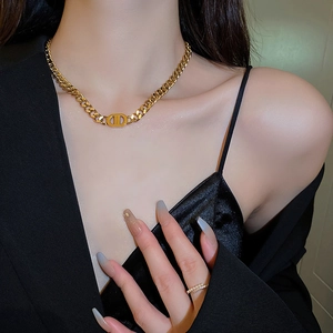 Detail of a golden cuban chain necklace with a signature CD charm on model neck