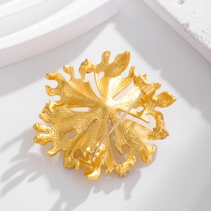 Golden coconut leaf brooch back view with secure rotary pin clasp on white prop