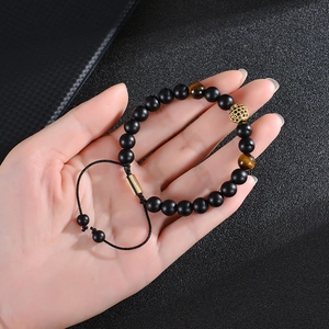 Tiger eye and matte black bead bracelet with gold zircon ball on hand with grey background