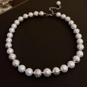 Irregular pearl and silver hollow bead necklace with adjustable clasp on dark surface
