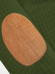 Close-up of dark green quilted fabric with brown suede oval elbow patches and precision stitching