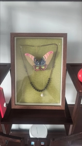 Detail view of a black beaded necklace with a white pearl drop pendant in a display frame