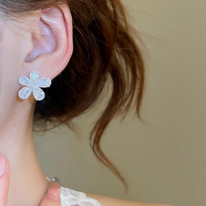 Close-up of a delicate white flower earring with a small pearl center on a female model