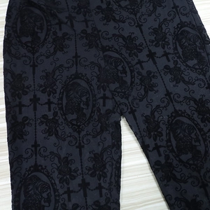 Detail of gothic lace flared trousers featuring cross and skull patterns on mesh fabric
