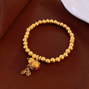 Macro view of a gold-plated beaded bracelet with hollow gourd and coin charms on silk