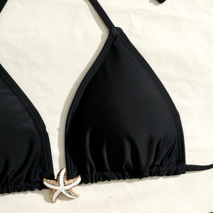 Detailed close-up of a black halter bikini top with a white starfish charm and gold edging