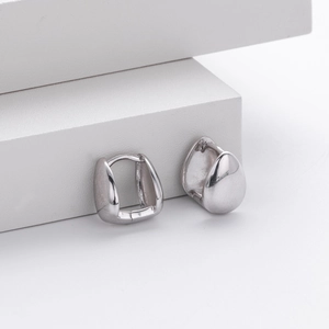 Macro detail of polished silver teardrop hoop earrings on minimalist geometric background