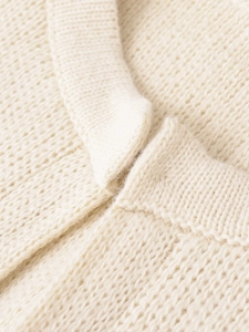 Dettaglio del collo a costine su maglione in maglia grossa color panna e trama tessuta