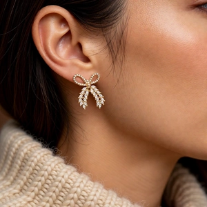Detailed close-up of golden bow earrings with zircons worn by a model on a beige sweater