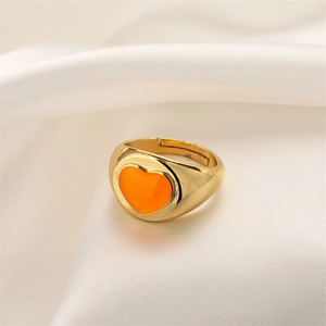 Detail of gold heart ring with orange enamel on elegant white silk background