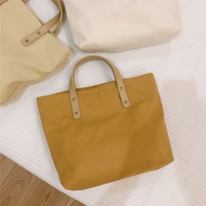 Close-up of three canvas tote bags in yellow and beige with reinforced metal rivet details