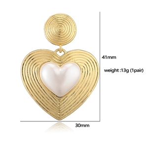 Detail view of gold heart earrings with white faux pearl and embossed sunburst texture