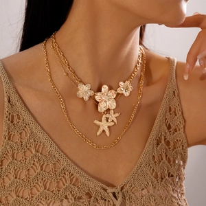 Close-up of gold layered necklace with metal flower pendants and starfish charms