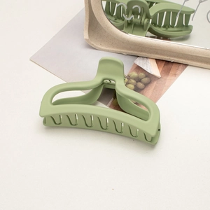 Close-up of matte light green hair claw clip with large grip teeth on white desk