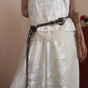 Detail of handmade woven waist chain featuring wooden rings and white beads on dress