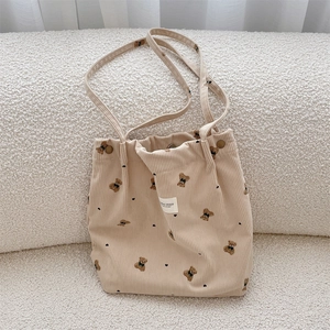 Close-up of beige corduroy tote bag with bear print and heart embroidery on white sofa