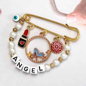 Close-up of golden evil eye safety pin brooch with ANGEL charms and pearl beads