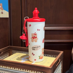 Detail of cute cartoon thermos with strawberry bear print and red strap in a cozy setting