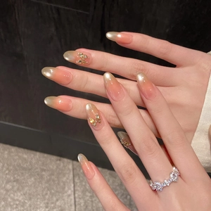 Macro detail of almond nails with peach gold gradient and 3D gold butterfly accents