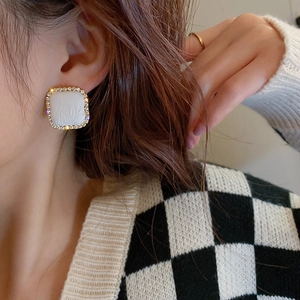 Close-up of a model wearing square houndstooth stud earrings with gold rim and rhinestones