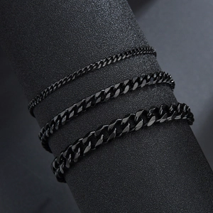 Close-up of three widths of black titanium steel Cuban link bracelets on a textured stand
