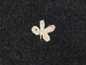 Macro detail of hand-stitched 3D floral embroidery on dark grey knit cardigan fabric